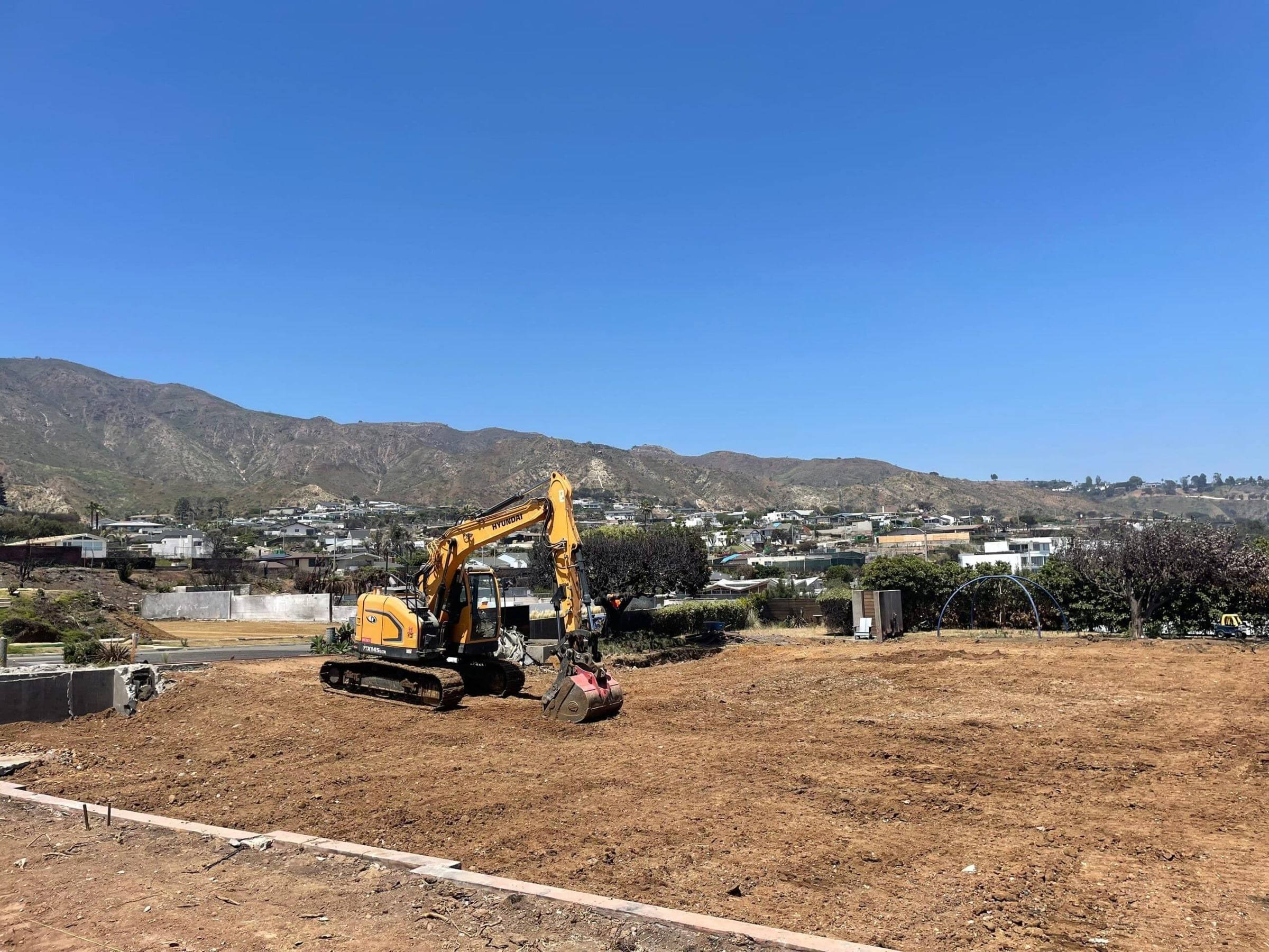 Excavator on a cleared Malibu lot with the Santa Monica Mountains behind