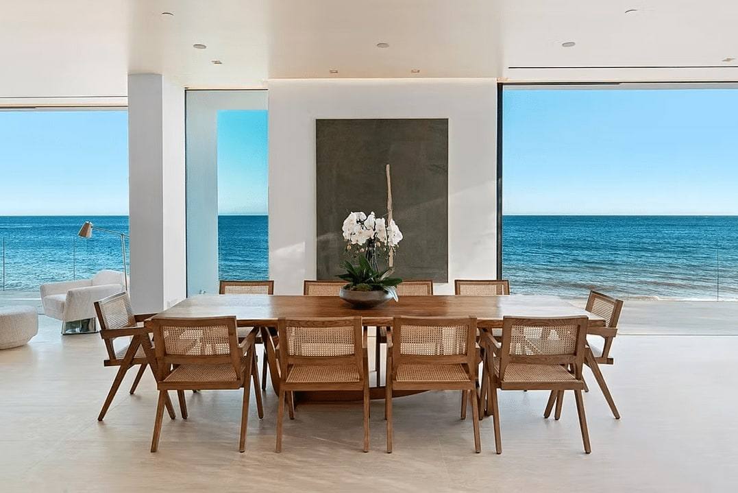 Dining table with rattan chairs in front of a glass wall facing the ocean