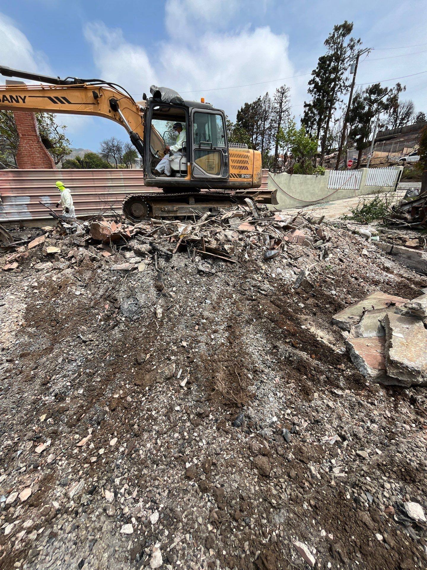 Excavator clearing burned debris on a fire-damaged lot in Pacific Palisades