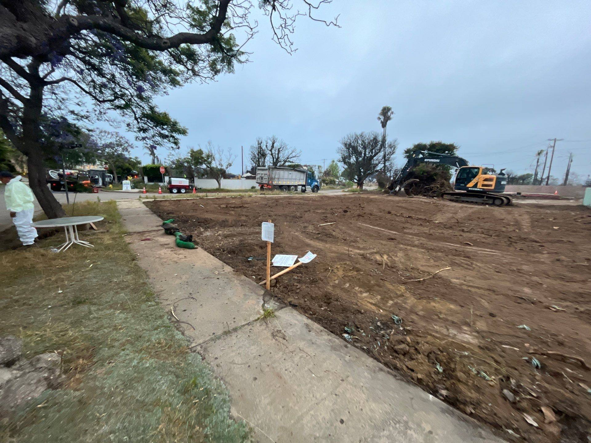 Cleared lot beside the sidewalk, with stakes and equipment at the far end