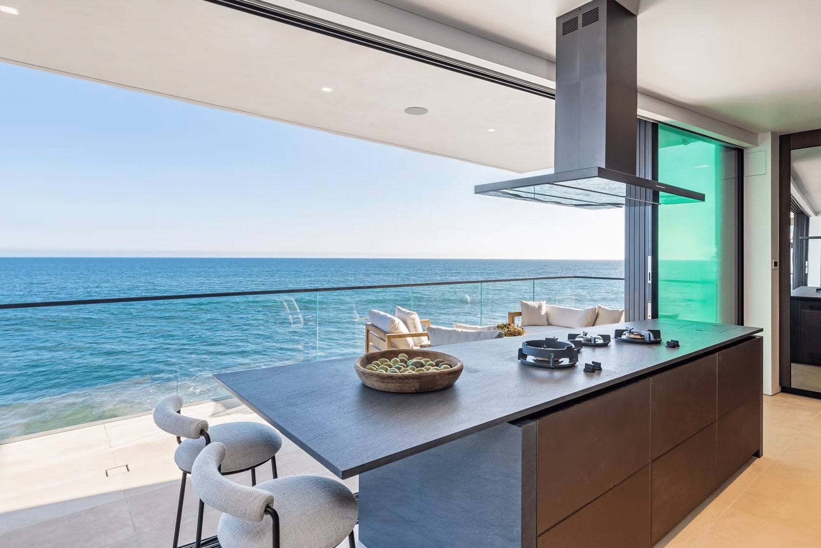 Kitchen island with a dark stone top and a steel hood, open to the ocean terrace