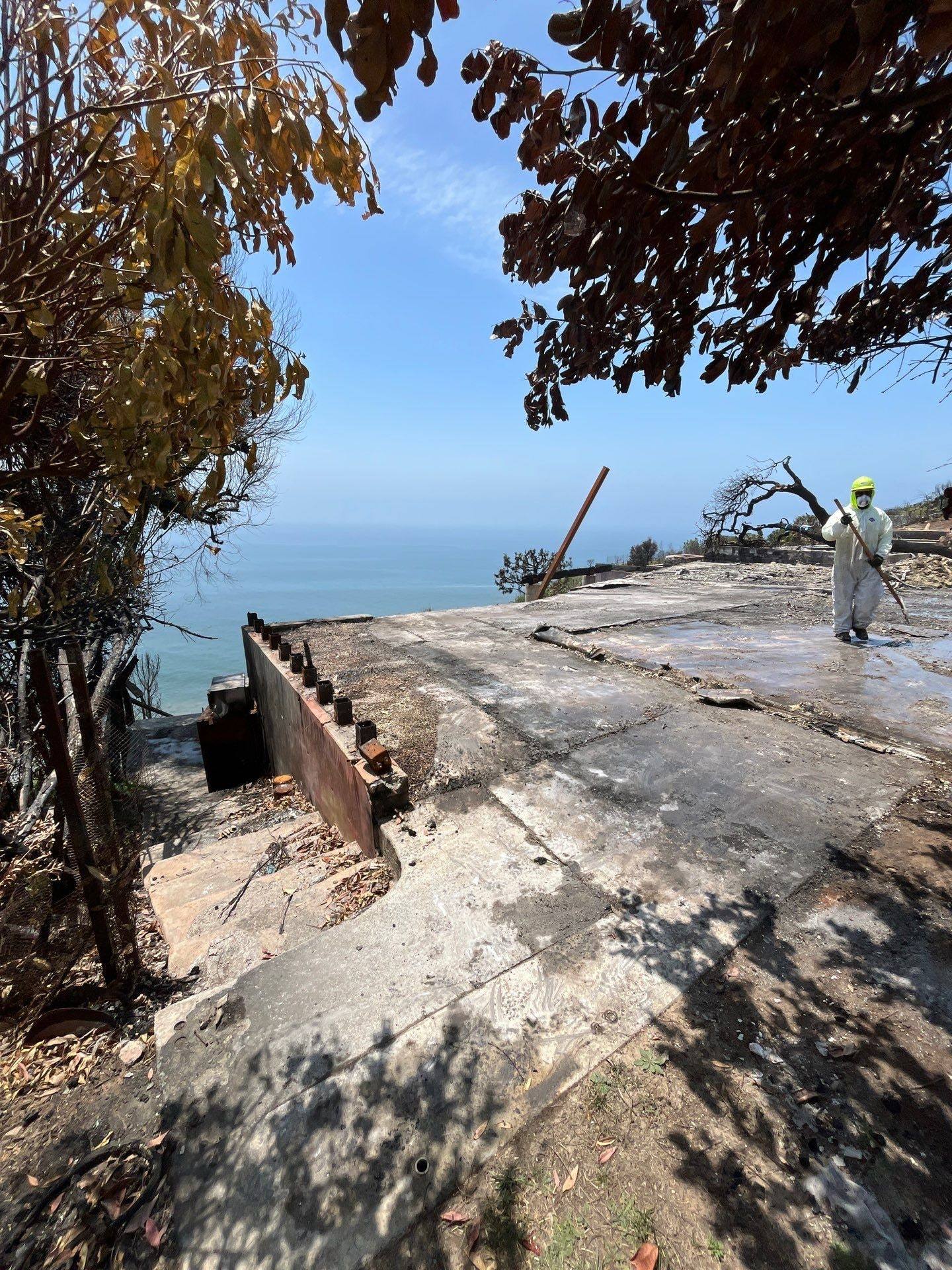 Crew member washing down a burned slab on a lot above the ocean
