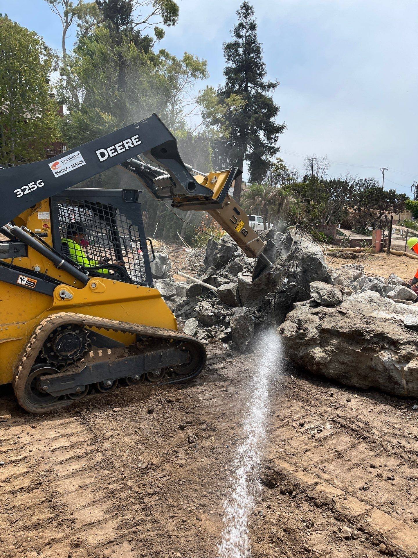 Track loader moving broken concrete while a crew member sprays water to keep the dust down