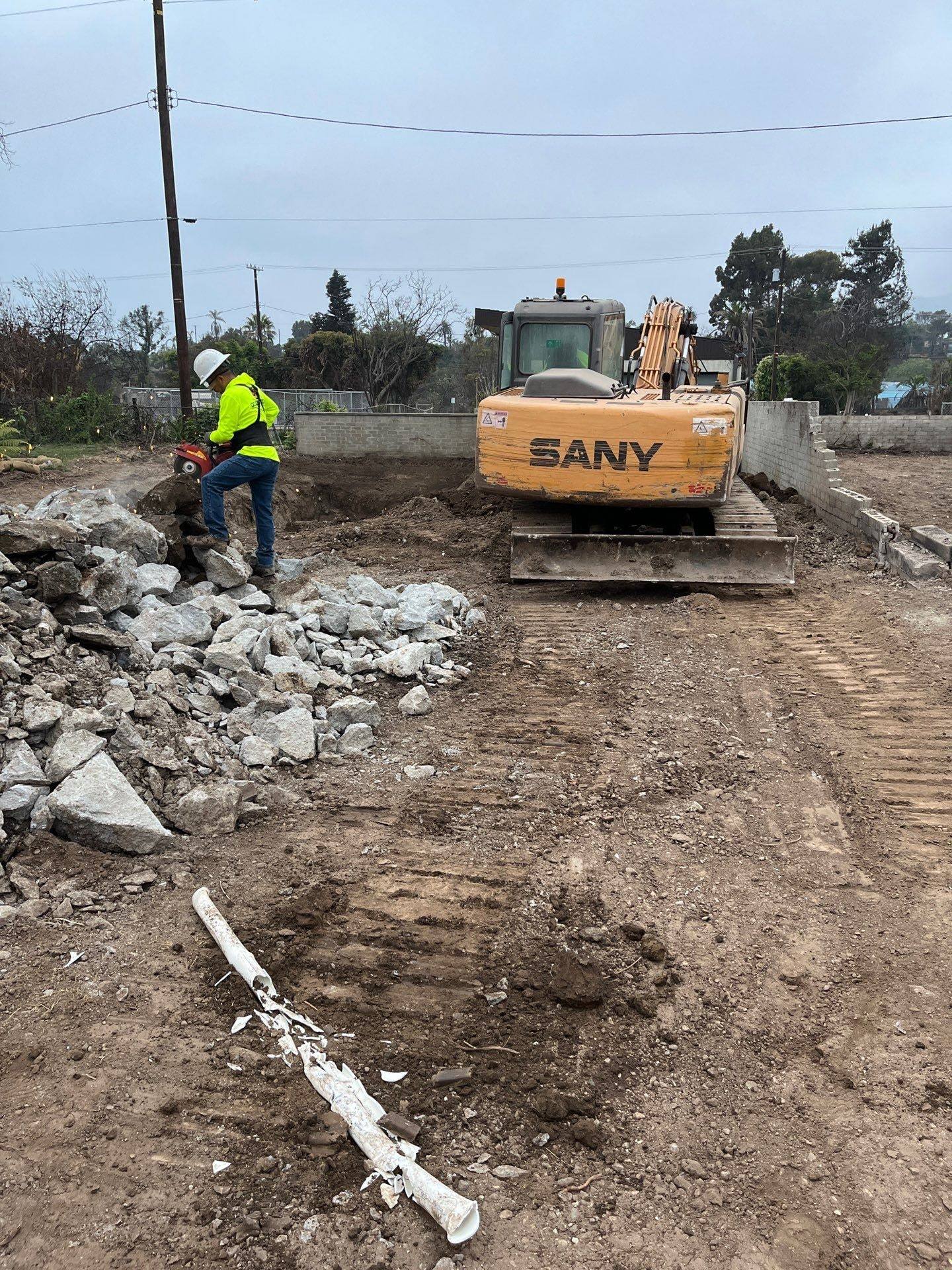 Crew member in high-visibility gear beside a compact excavator and a pile of broken concrete